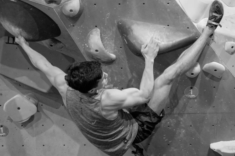 Black-and-white shot from above of a climber bridging between large holds on a bouldering wall