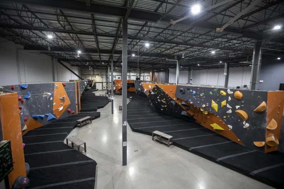 Long rows of orange and grey bouldering walls over thick black matting in a large hall