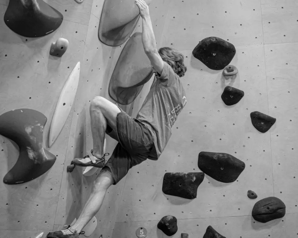 Black-and-white shot of a climber hanging from a large sloper on a plywood bouldering wall