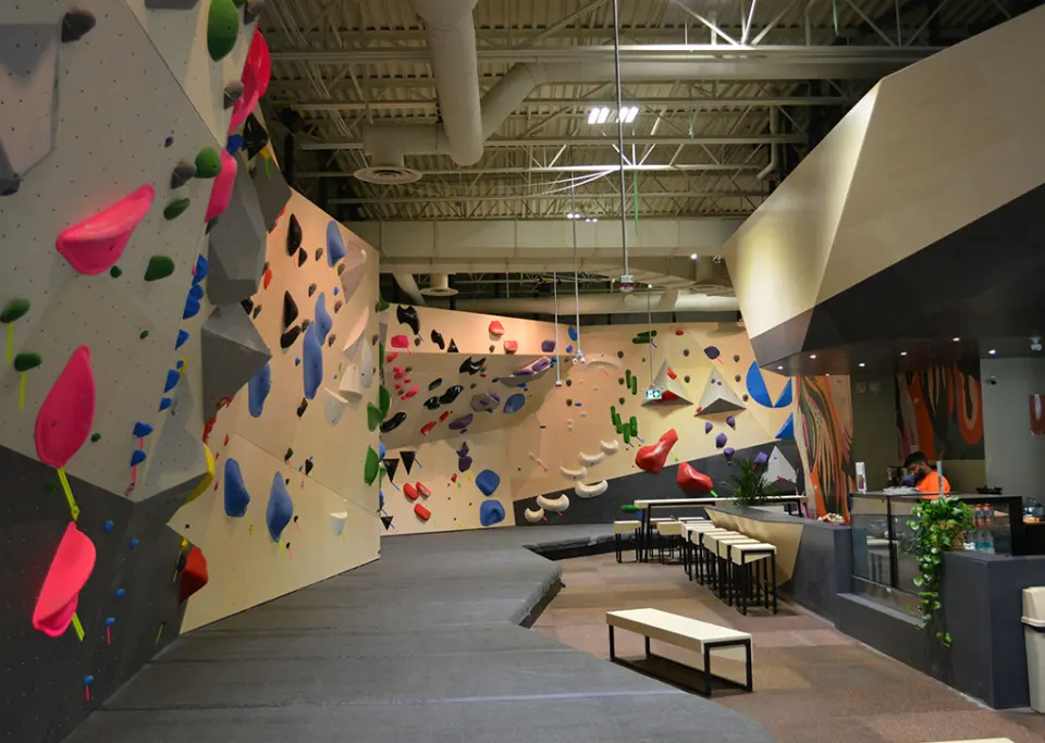 Pale wooden bouldering walls with colourful holds beside the bistro counter and bar stools