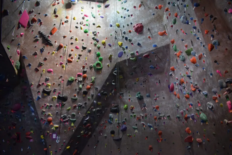 Tall textured roped wall covered in holds and route tape, with top ropes hanging down