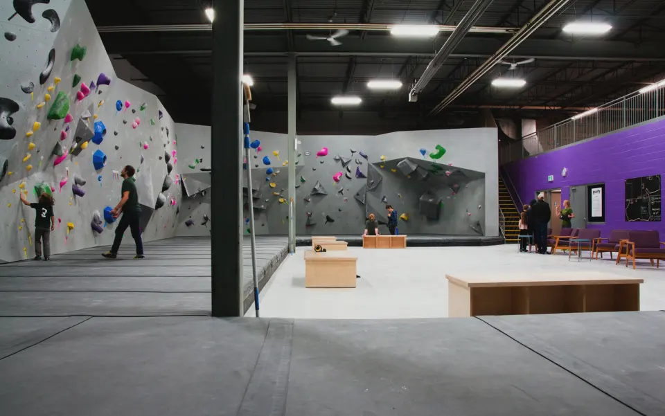 Grey bouldering walls around a matted floor, with a seating area by a purple wall