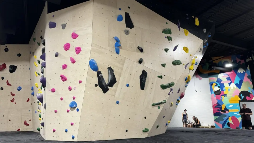 Plywood bouldering walls with colourful holds and a bright mural on the back wall