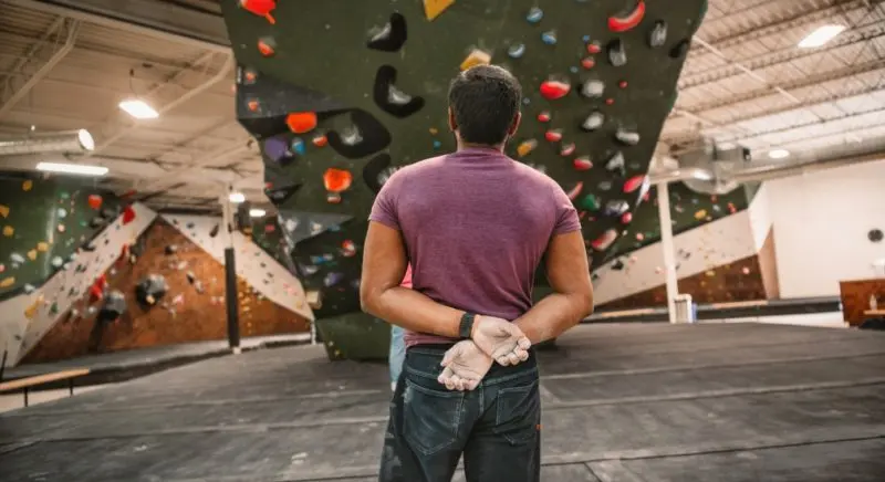 Climber looking up at a steep green bouldering wall with colourful holds