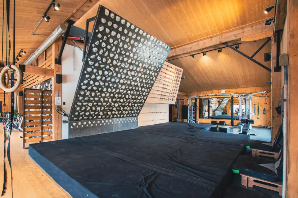 Kilter Board and campus rungs above deep matting in a wood-panelled training room
