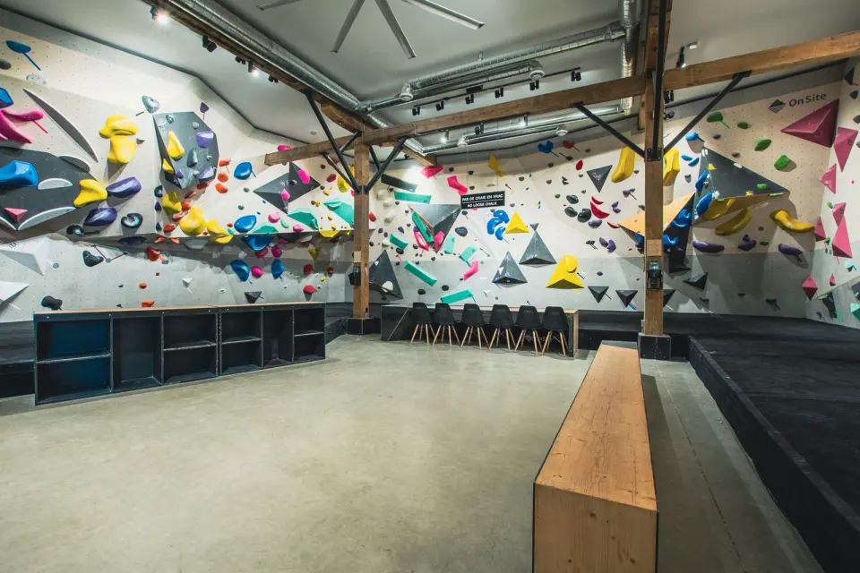 Bouldering walls with bright holds and grey volumes above black matting and cubby shelves