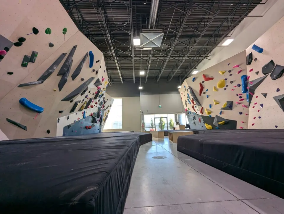 Two angled bouldering walls with colourful holds either side of a walkway between thick black mats