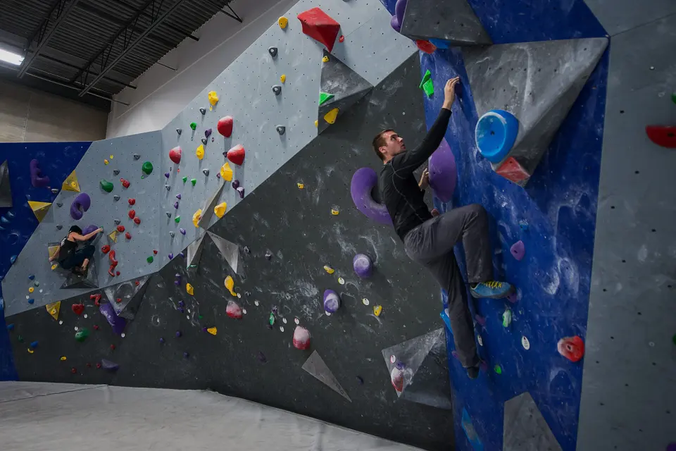 Climbers on a long grey and blue bouldering wall with angled panels and colourful holds
