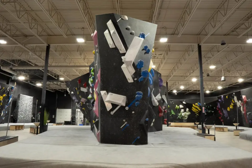 Freestanding black boulder with white volumes in a large matted bouldering hall