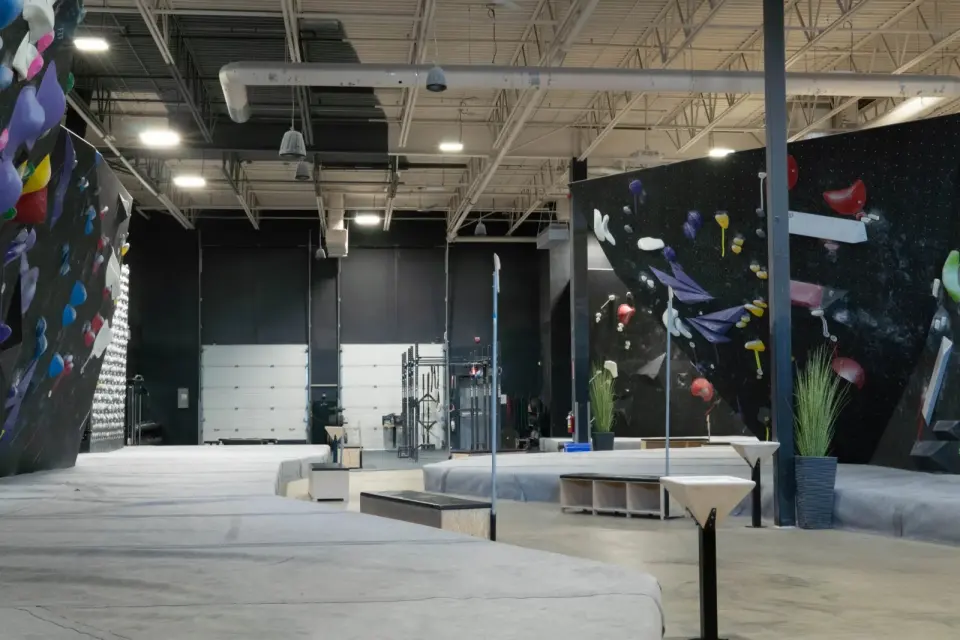Wide view of the bouldering hall with black walls and thick grey matting