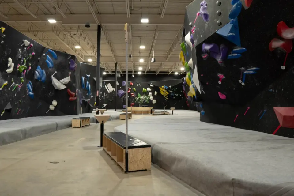 Matted aisle between bouldering walls, with wooden benches