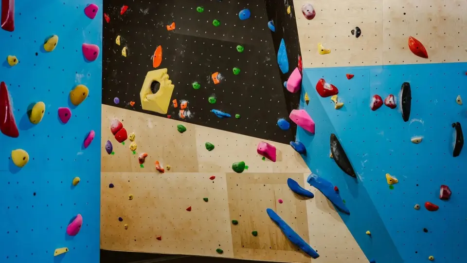 Blue, black and plywood bouldering walls set with colourful holds and a yellow volume