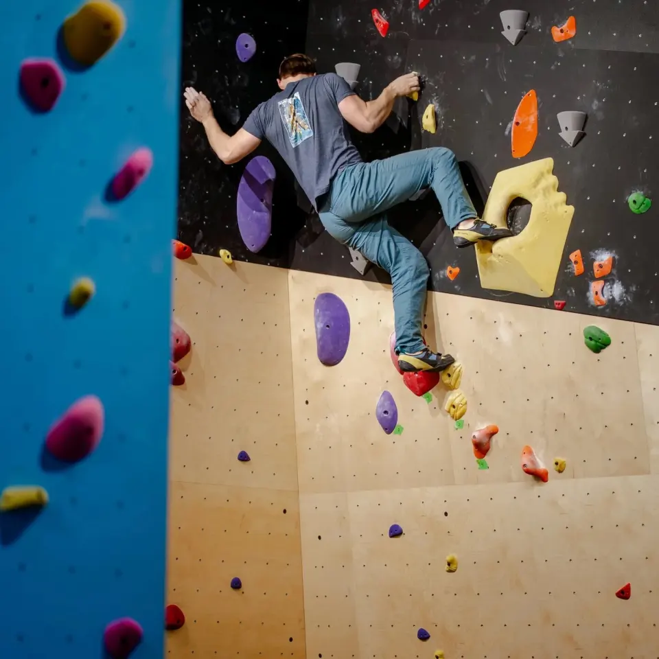 Climber stepping onto a yellow volume where a plywood wall meets a black overhang