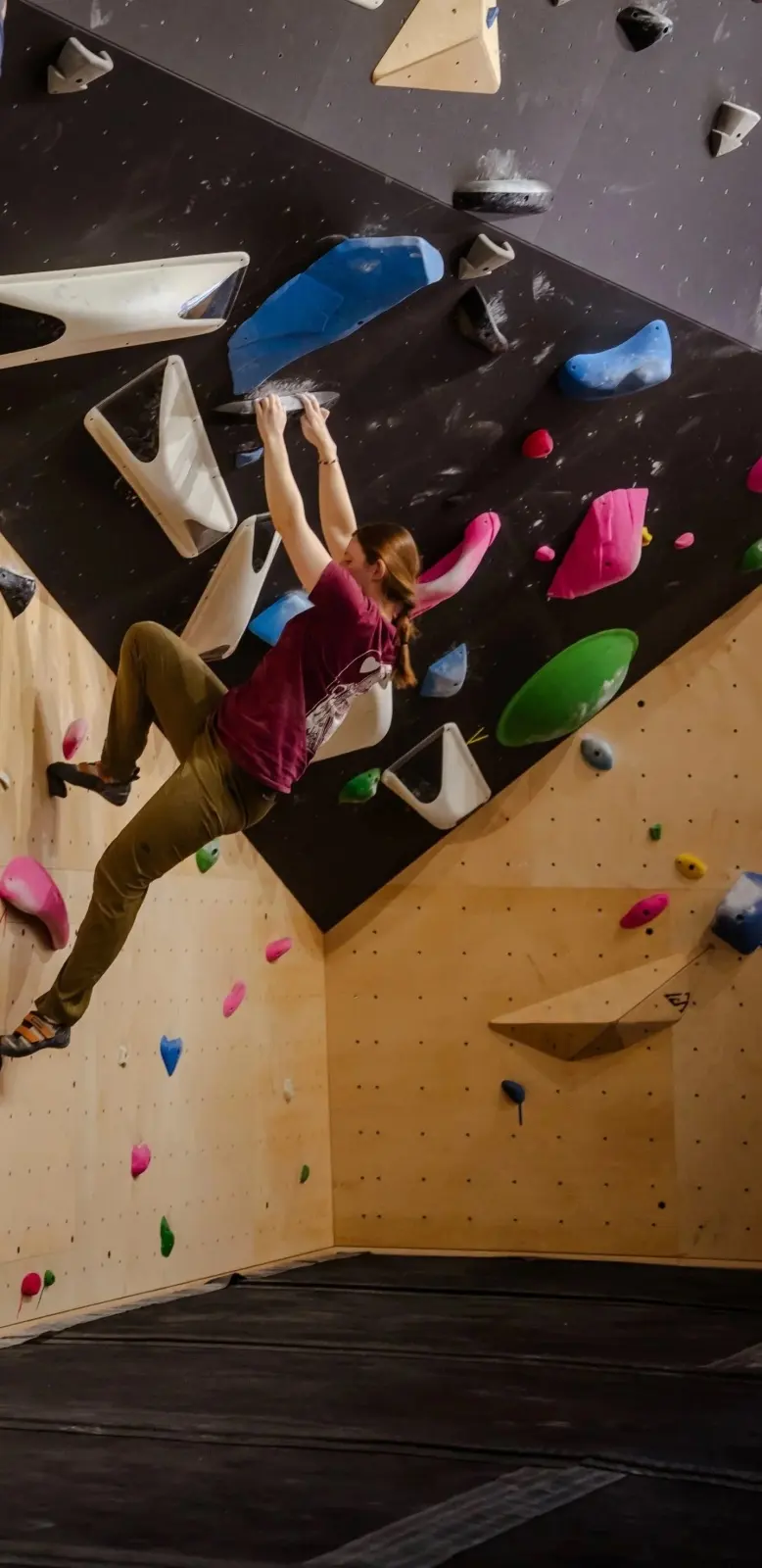 Climber hanging from white volumes on a steep black wall above plywood panels