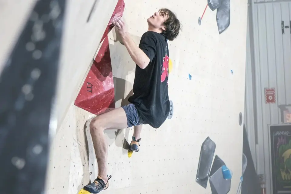 Climber pulling on a red volume on a leaning white bouldering wall