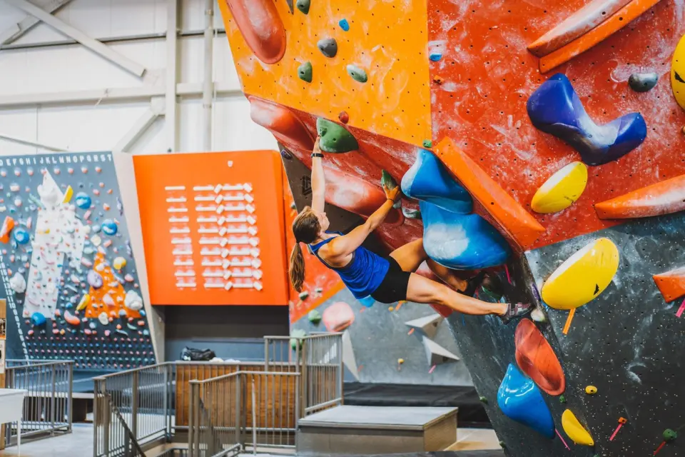 Climber on a steep bouldering wall with big colourful volumes