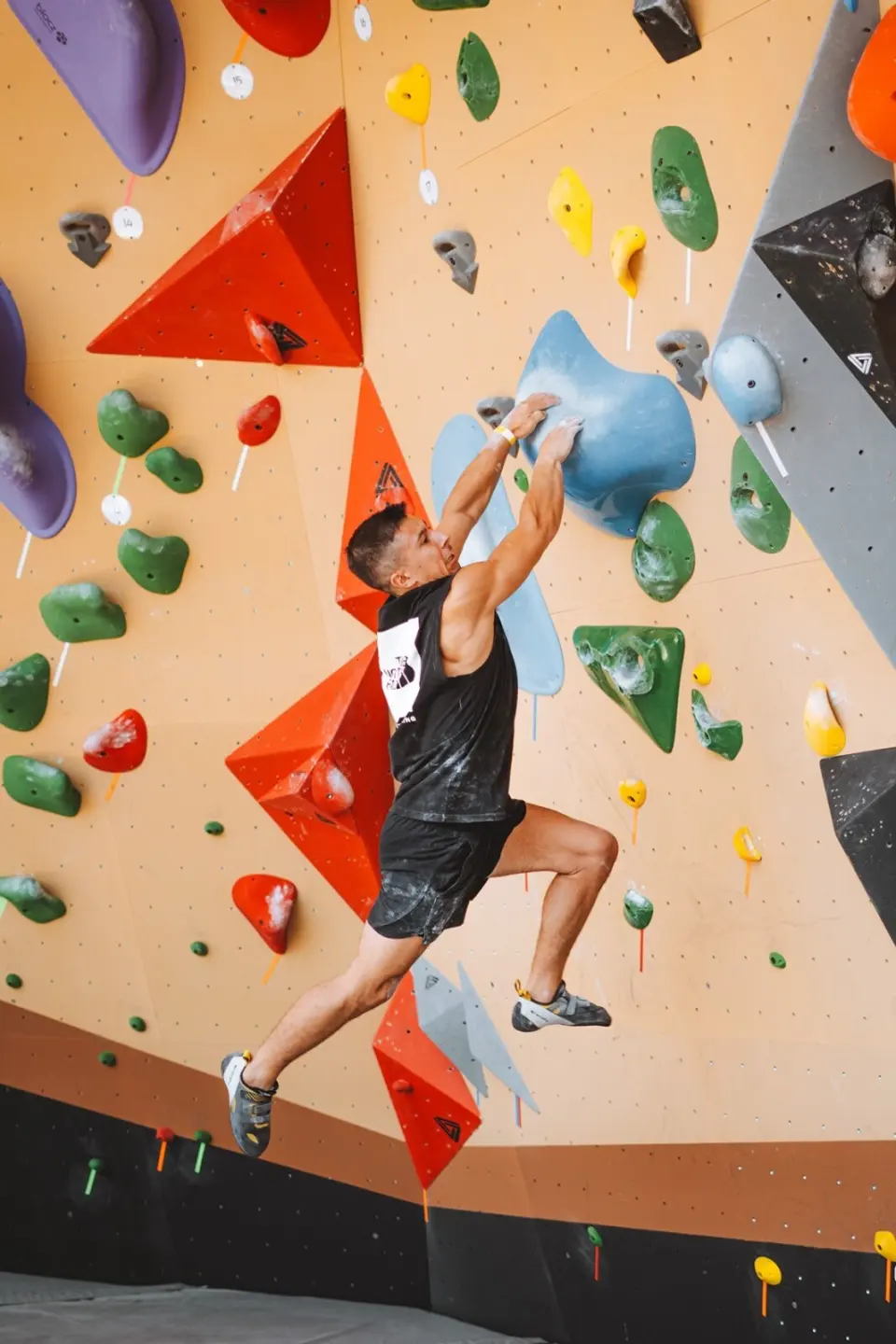 Climber reaching between red volumes on an orange bouldering wall
