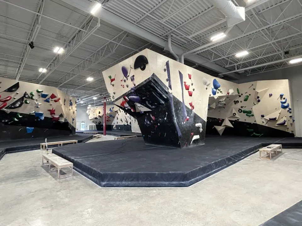 Central boulder with dark overhangs on a matted island in a bright bouldering hall
