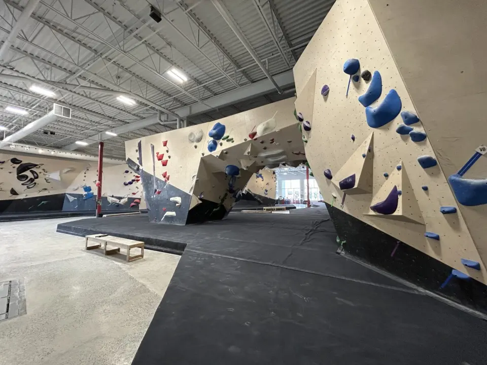 Angled bouldering walls with blue and white holds above thick black matting