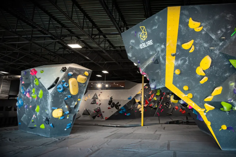 Freestanding boulder and a steep overhang with a yellow stripe and the Délire logo above grey mats