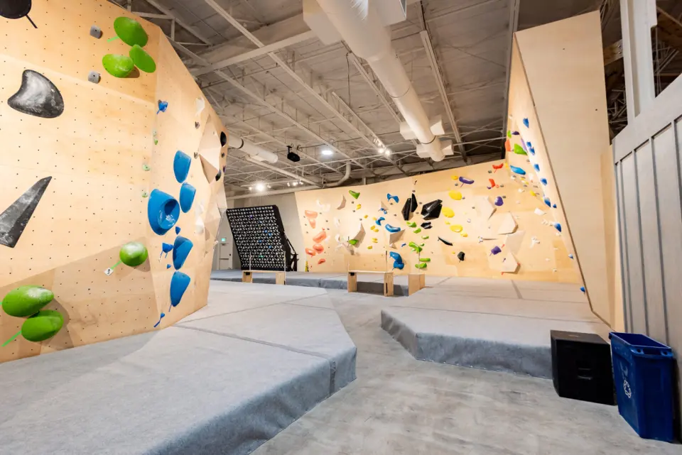 Wooden bouldering walls around matted islands, with a black training board at the back