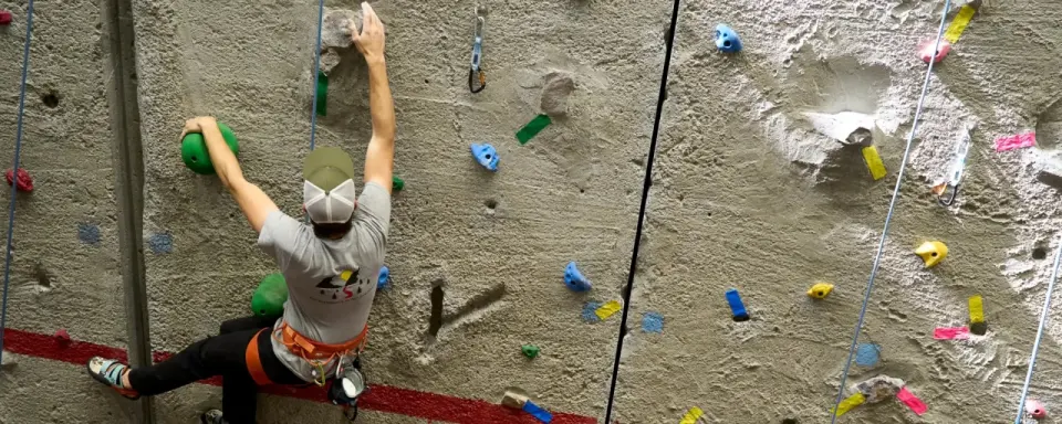 Climber on the concrete rope wall, with quartzite holds, cracks and taped routes