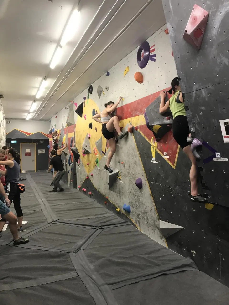 Climbers on the painted walls of the basement bouldering area, above thick matting