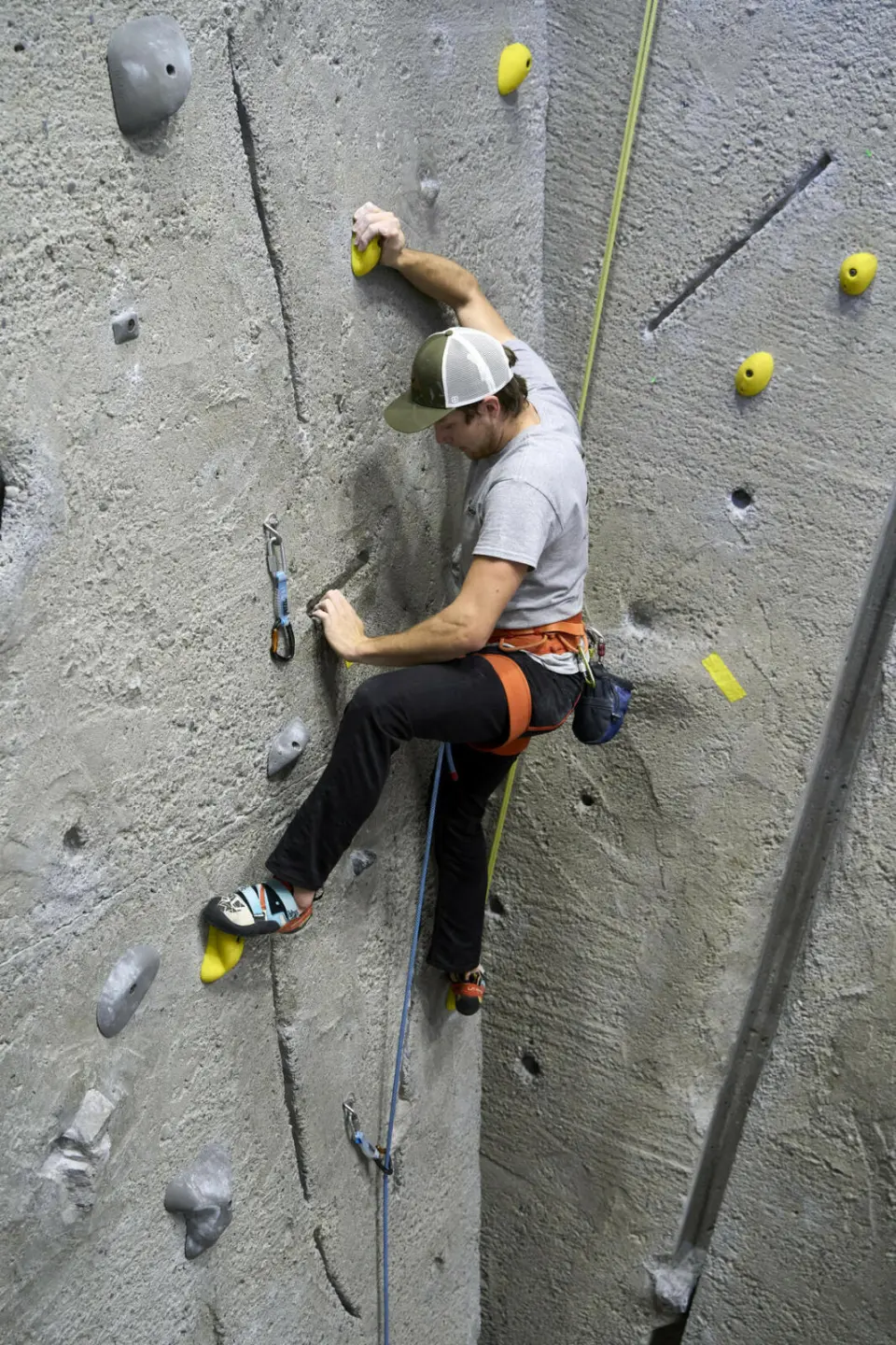 Lead climber on the textured concrete wall, beside a quickdraw and a crack