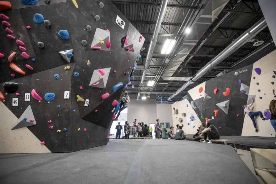 Bouldering hall with a large black feature wall, grey matting and climbers resting by the walls