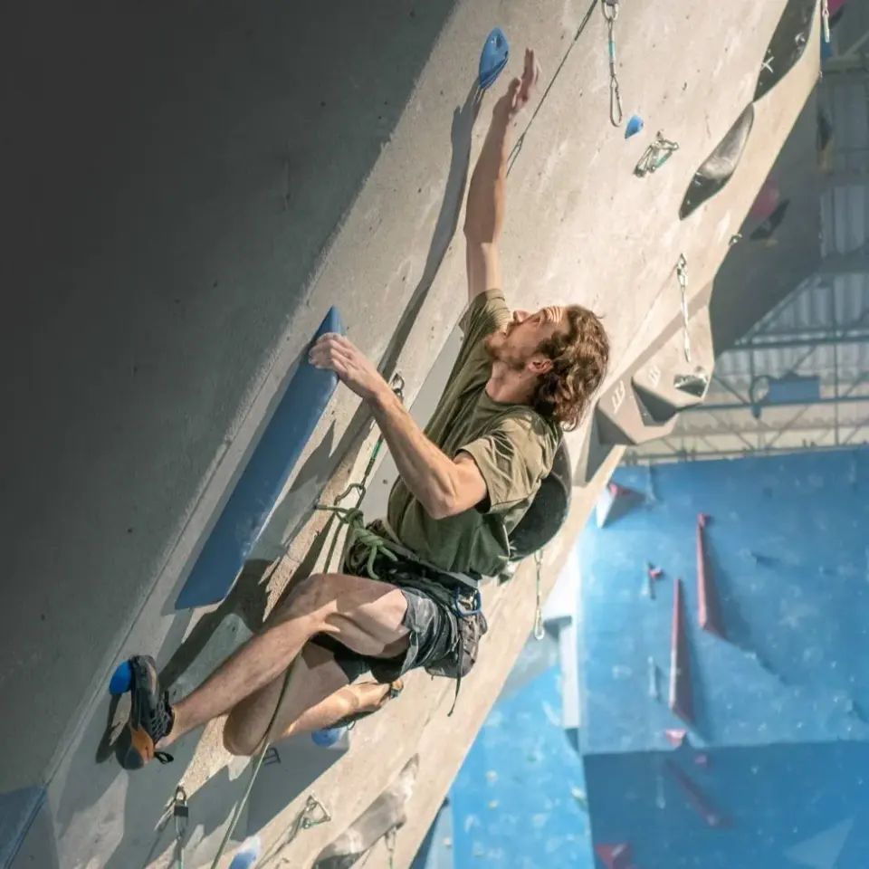Climber leading up a steep grey overhang, with blue walls behind