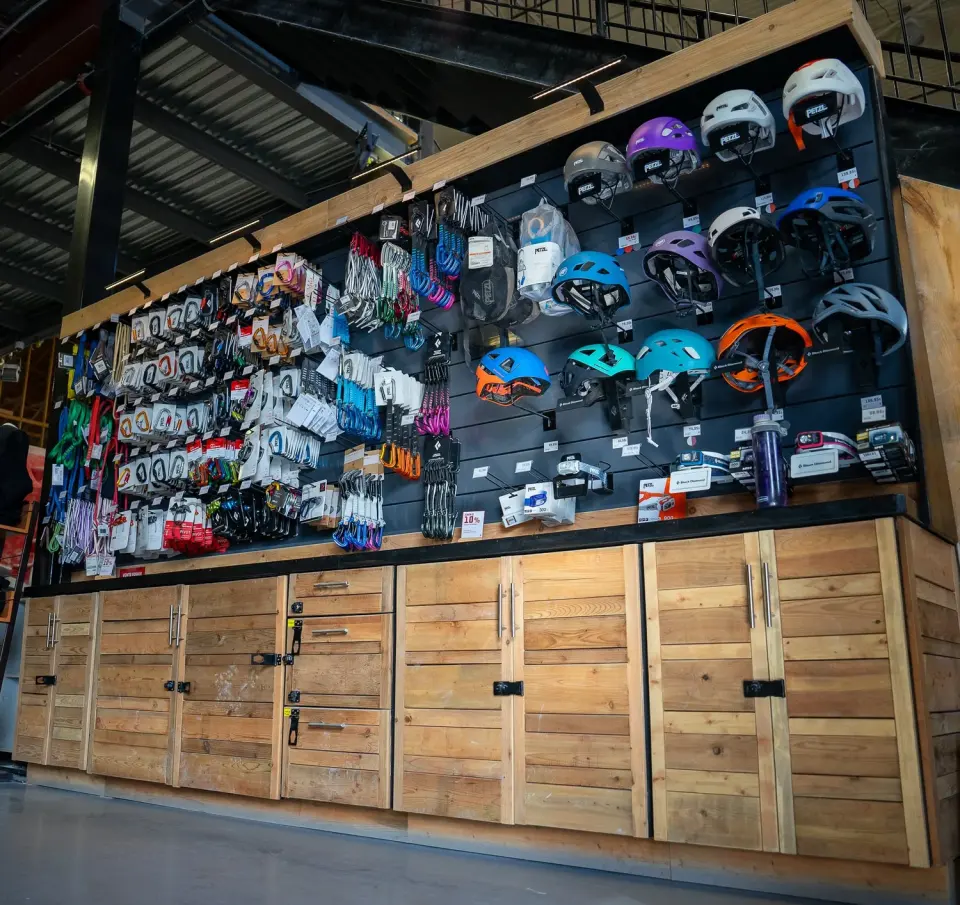 Shop wall of climbing helmets, quickdraws, carabiners and slings above wooden cabinets