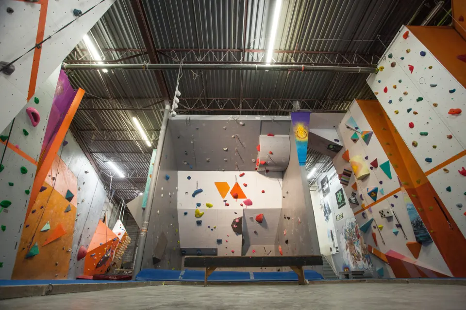 Empty climbing hall with tall roped walls and a bouldering alcove under a steel roof