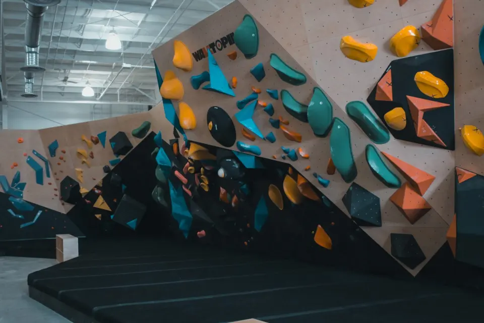 Angled bouldering wall with colourful volumes above black matting