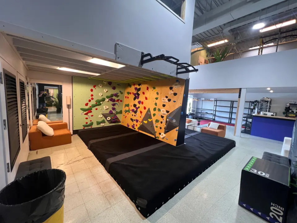 Low bouldering wall under the mezzanine, with armchairs beside it and the front desk behind
