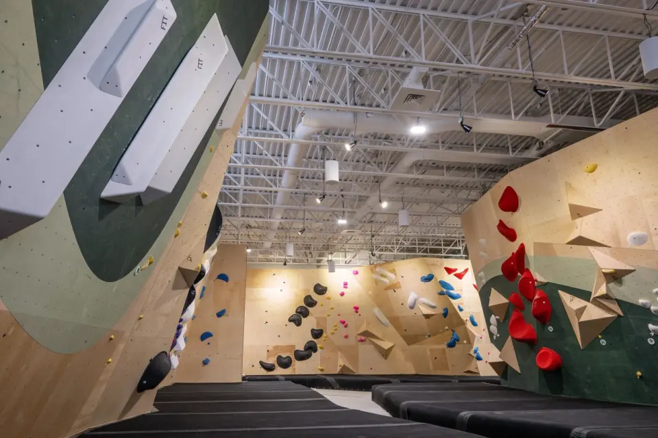 Plywood and green bouldering walls with red, blue and black holds above thick black matting