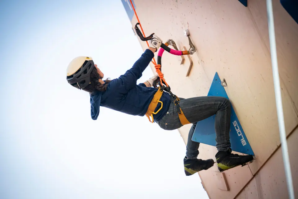 Climber with ice tools and crampons on a tall plywood dry-tooling wall