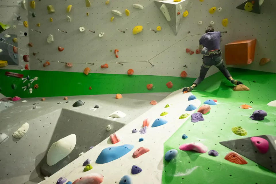 Lead climber traversing above angled slab boulders covered in colourful holds