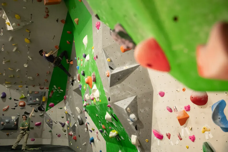 Lead climber clipping quickdraws on a steep wall while a belayer watches from below