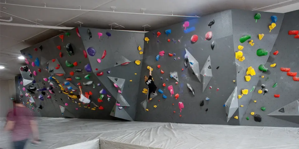 Climbers on the long grey bouldering wall above thick matting