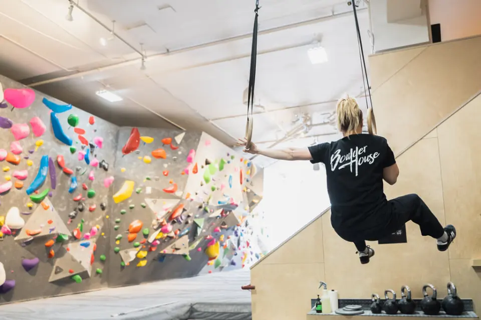 Climber training on gymnastic rings beside the bouldering wall and kettlebells