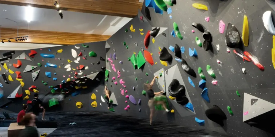 Climbers on the long grey bouldering wall under a timber ceiling