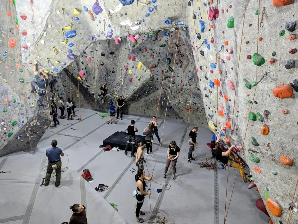 Climbers and belayers on the tall textured roped walls, seen from above