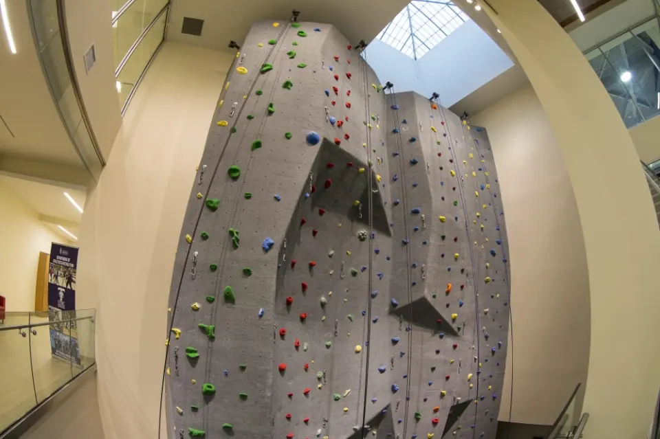 Tall grey climbing wall with top ropes and coloured holds under a skylight