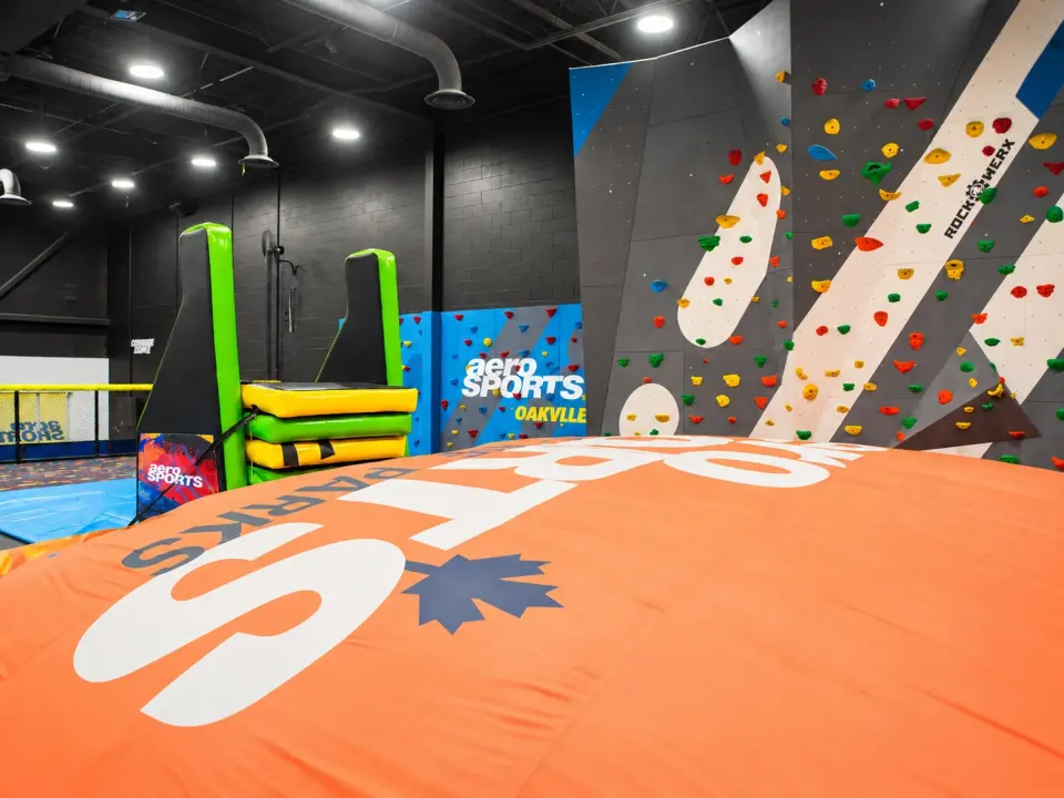 Grey and white climbing walls with coloured holds behind an orange inflatable landing