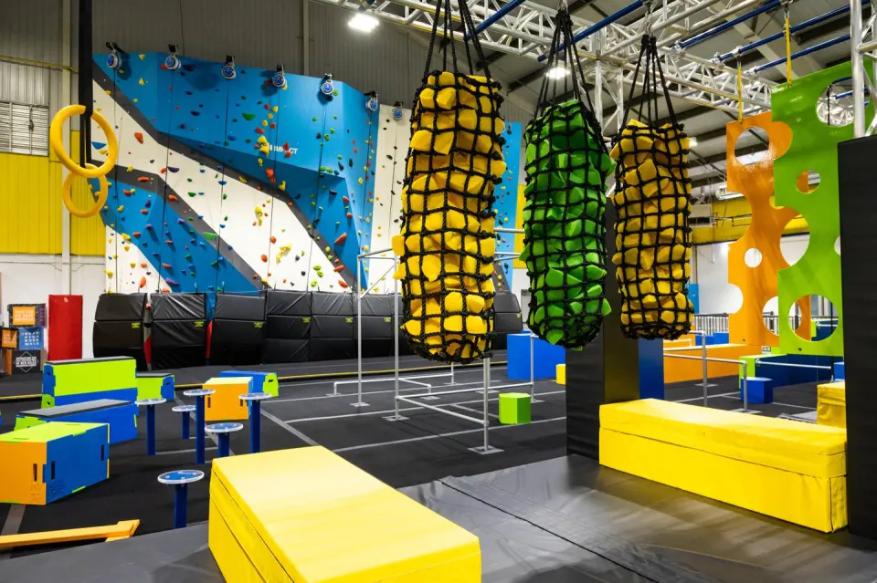 Climbing wall with auto-belays seen past hanging ninja course obstacles