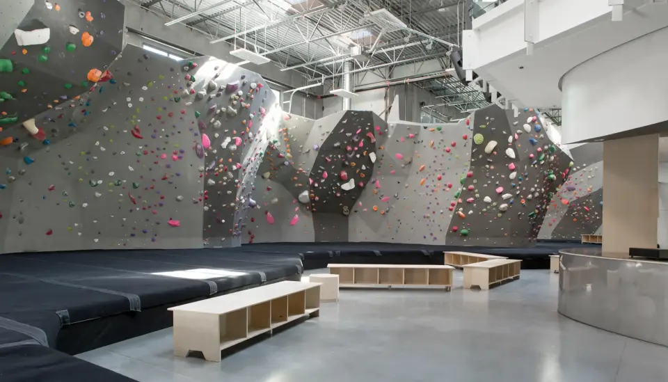 Wide bouldering hall with grey and black walls, deep matting and wooden benches at Hive North Shore