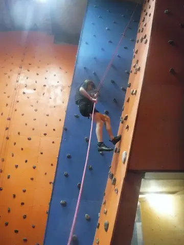 Person abseiling down a blue climbing wall between orange walls