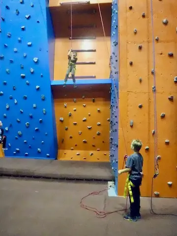 Blue and orange roped climbing walls beside a ladder up to a high platform