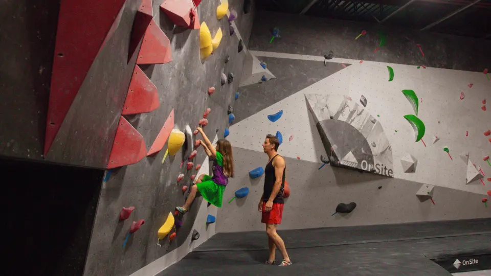 Adult watching a child climb a steep wall with red volumes