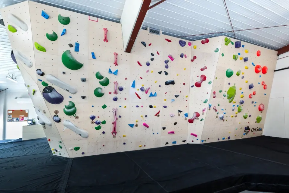 Long plywood bouldering wall set with colourful holds over thick black matting